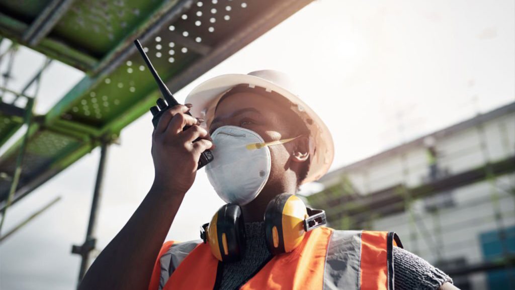 African man in industrial PPE. White hardhat, range reflector talking on a walkie talkie