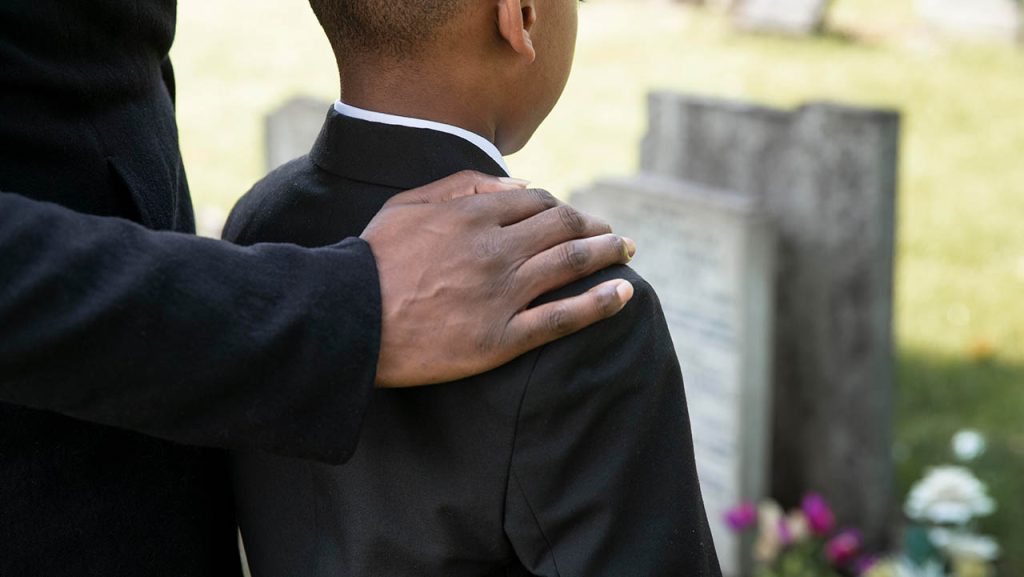 Hand of an older man on the shoulder on the shoulder of a young boy dressed in a black suit at a funeral