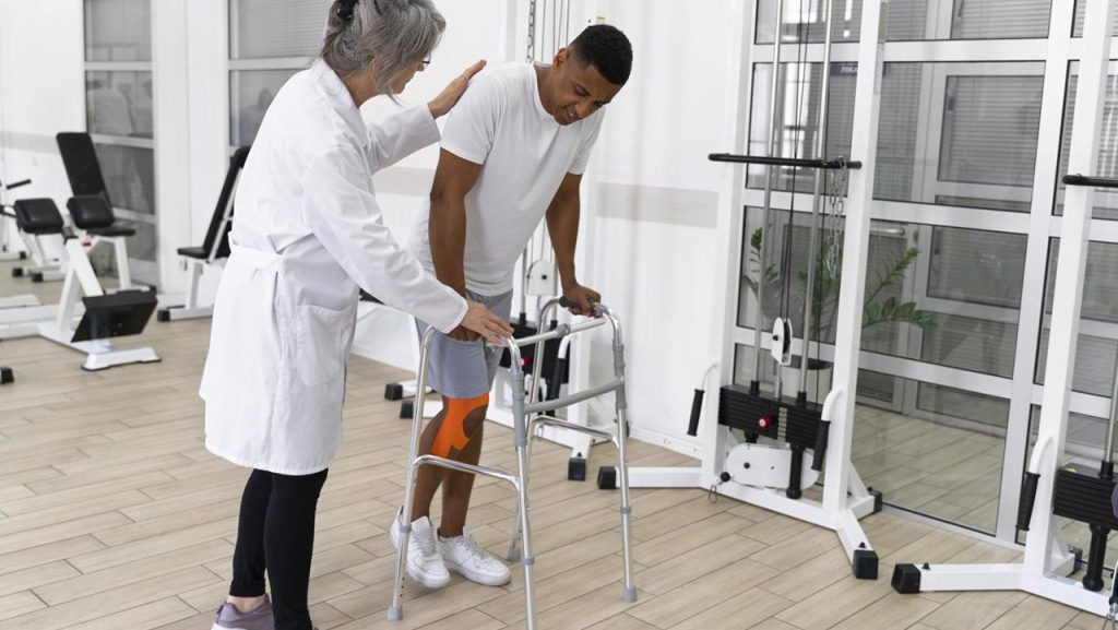 Man in physical rehabilitation trying to walk with the assistance of a doctor.